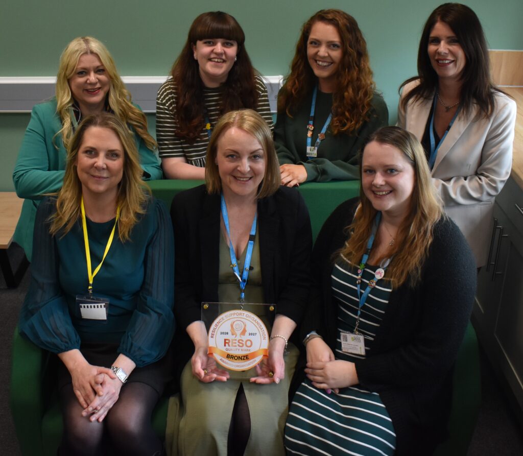 Group of diverse Suffolk New College staff members smiling and celebrating an award, showcasing teamwork and success in education.
