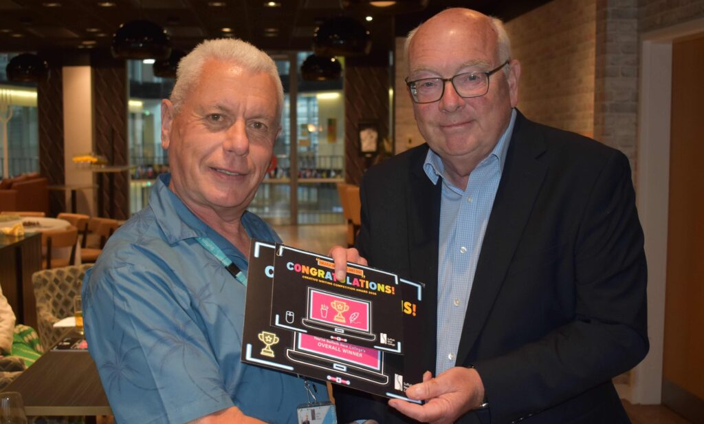 Two men at Suffolk New College holding a congratulatory award plaque, smiling and celebrating success in a modern, well-lit indoor setting.