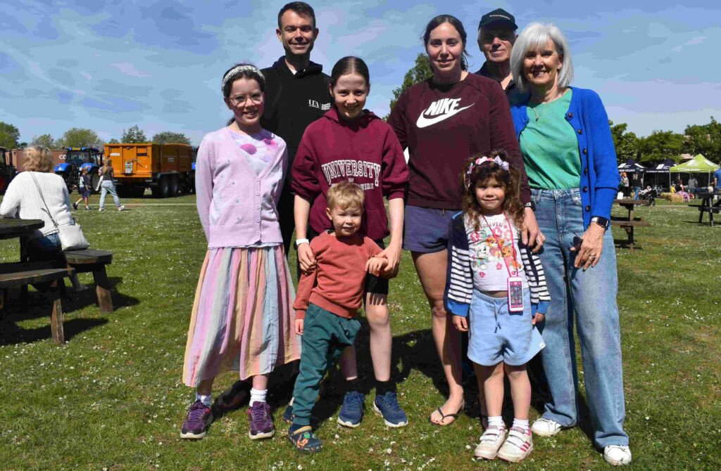 Group of children and adults smiling and posing together outdoors during Suffolk New College family fun day in sunny weather.