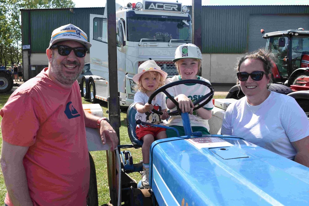 Family enjoying a sunny day at Suffolk New College's annual fun day, with children on a tractor ride and adults smiling, highlighting community and outdoor activities.