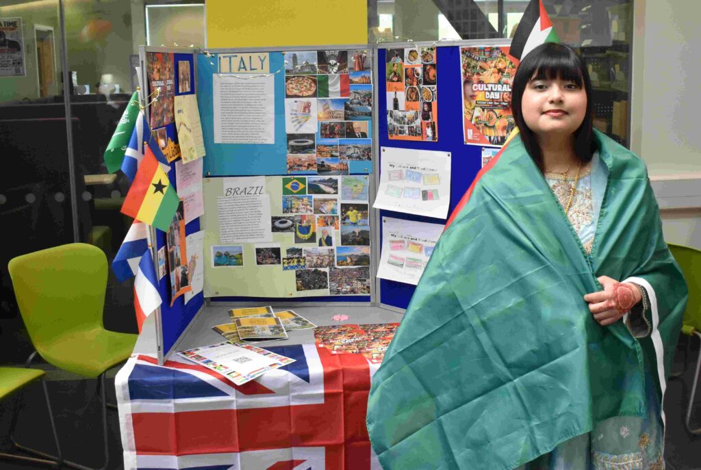 Student representing Ghana with a flag and traditional attire at Suffolk New College during an international culture event, showcasing diverse global cultures and educational activities.