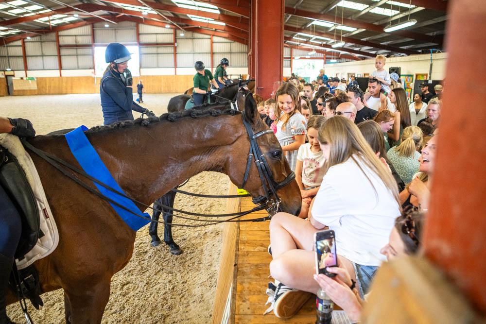 Children and families enjoying horse riding and interactive activities at Suffolk New College's annual family fun day, with a lively indoor arena and enthusiastic participants.