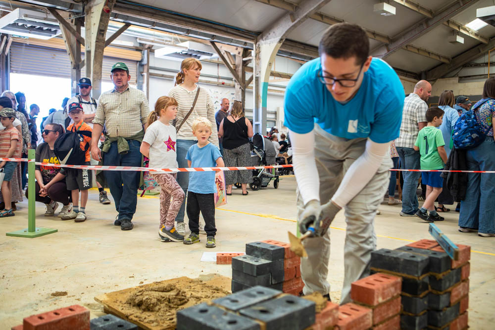 Family enjoying Suffolk New College's annual fun day with children and adults participating in outdoor activities inside a large covered space.