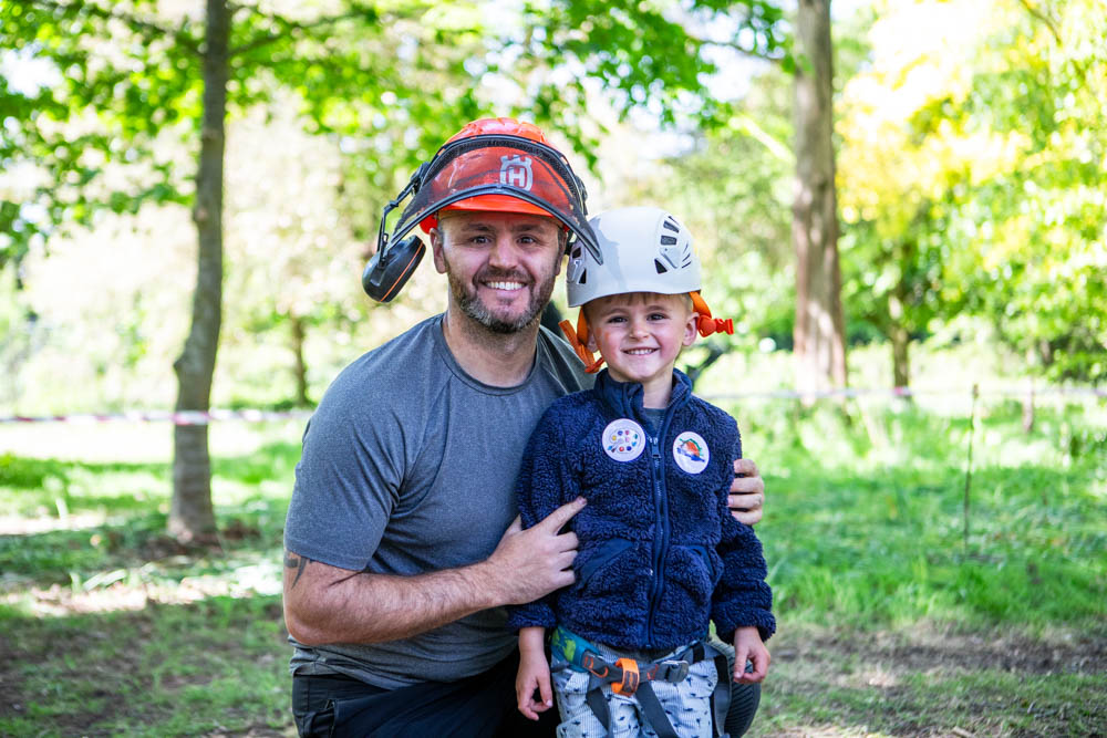 A father and daughter enjoying outdoor activities at Suffolk New College's family fun day, surrounded by lush green trees and sunshine, promoting community engagement and outdoor learning.
