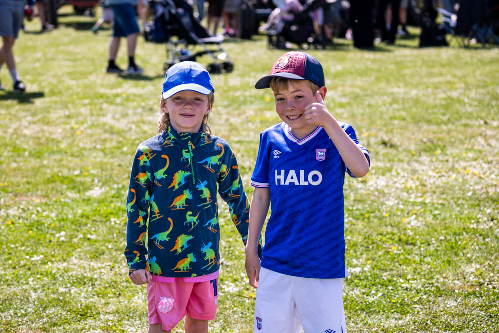 Two children enjoying the sunshine at Suffolk New College's annual family fun day, with families and activities visible in the background. Perfect for community and outdoor event keywords.