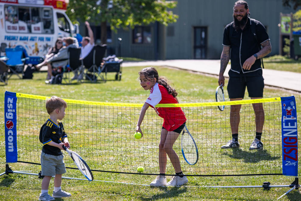 Children playing tennis during Suffolk New College's family fun day event on a sunny day, with families and staff enjoying outdoor activities.
