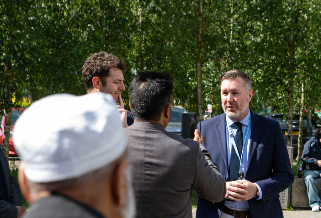 Group of diverse students and staff engaging in a discussion outdoors at Suffolk New College campus, with trees and benches in the background, promoting education and community.