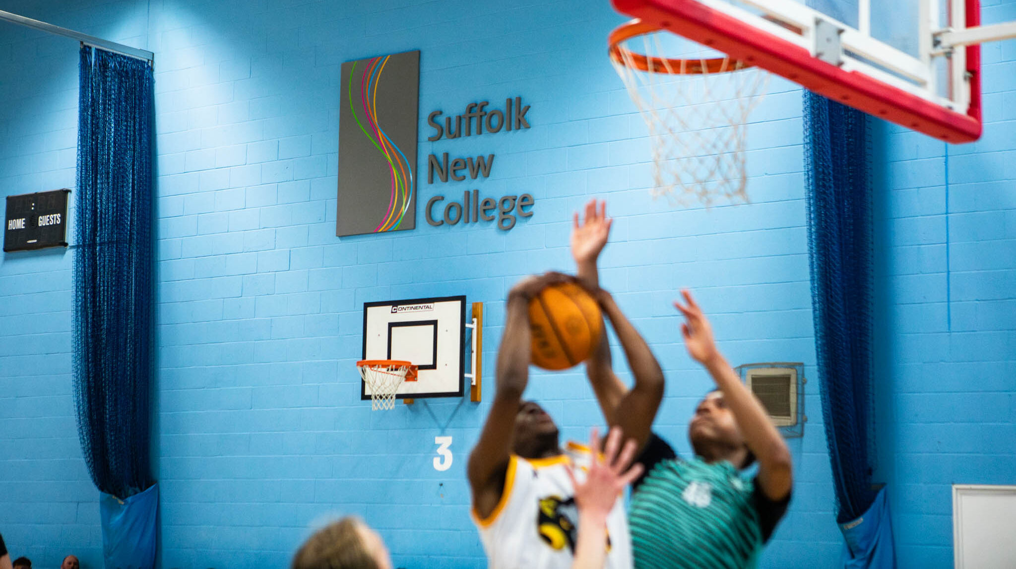 Students playing basketball in a Suffolk New College gymnasium, demonstrating sports facilities and active student engagement in sports education.
