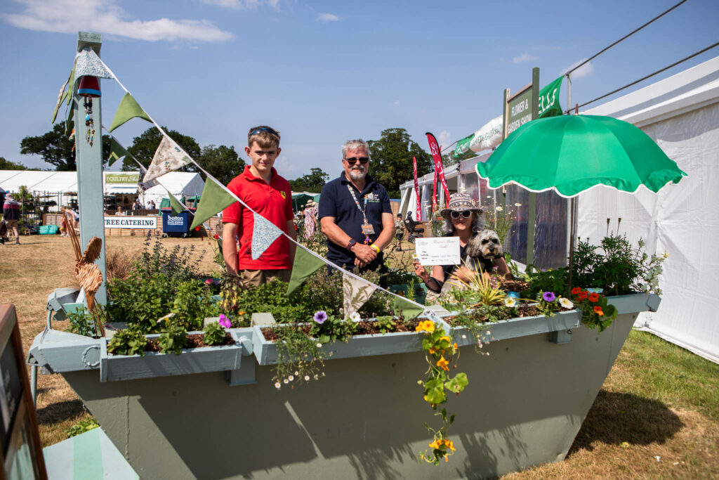Students and staff at Suffolk New College showcasing a creative garden project in a boat-shaped planter, highlighting college's focus on horticulture and community engagement.