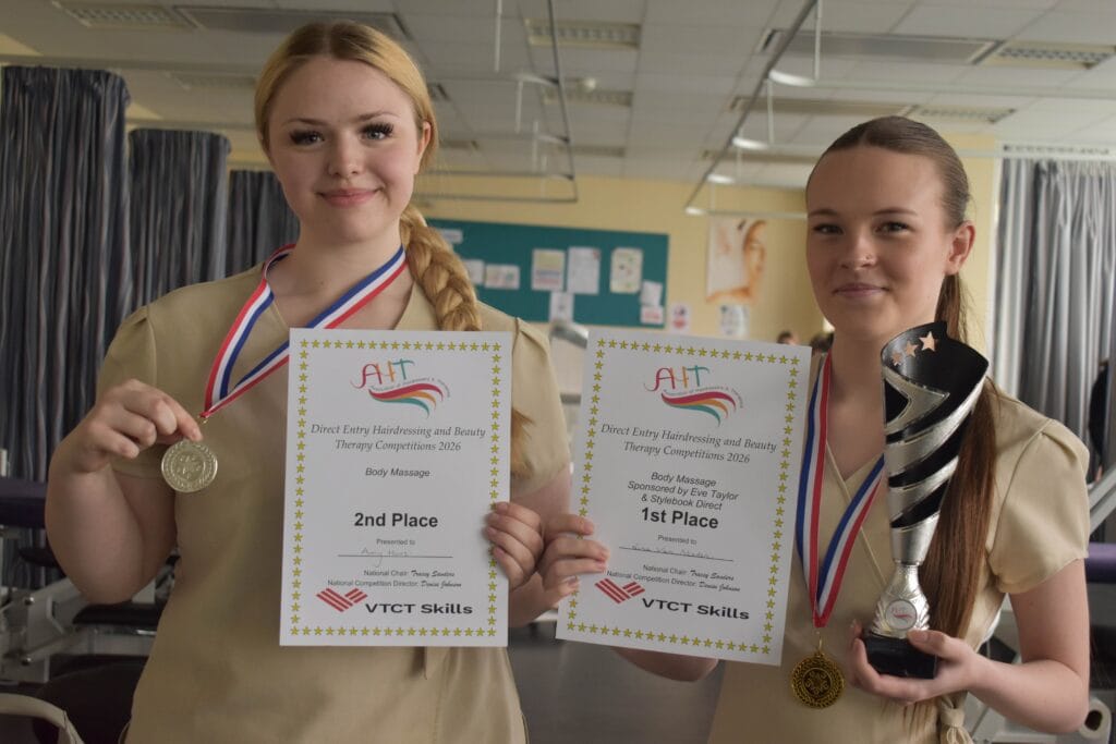 Two young female students at Suffolk New College holding awards and medals, celebrating their achievements in a classroom setting.
