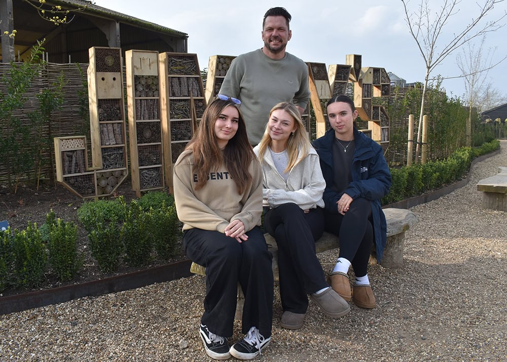 Group of three students sitting on a bench with a teacher at Suffolk New College, showcasing modern outdoor learning spaces and student engagement in a vibrant college environment.
