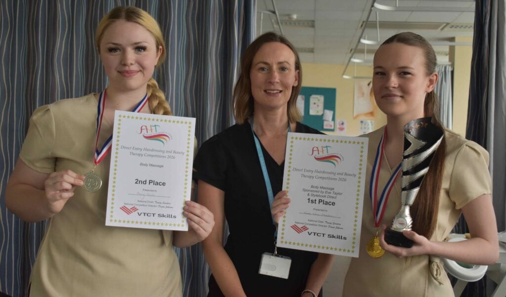 Two female students and a staff member at Suffolk New College holding awards and medals during a recognition event, celebrating academic achievements and skills development.