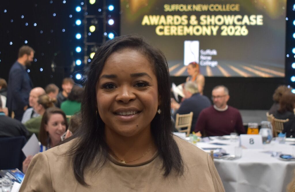 Smiling student at Suffolk New College awards ceremony with a lively crowd and stage in the background, celebrating student achievements in 2026.