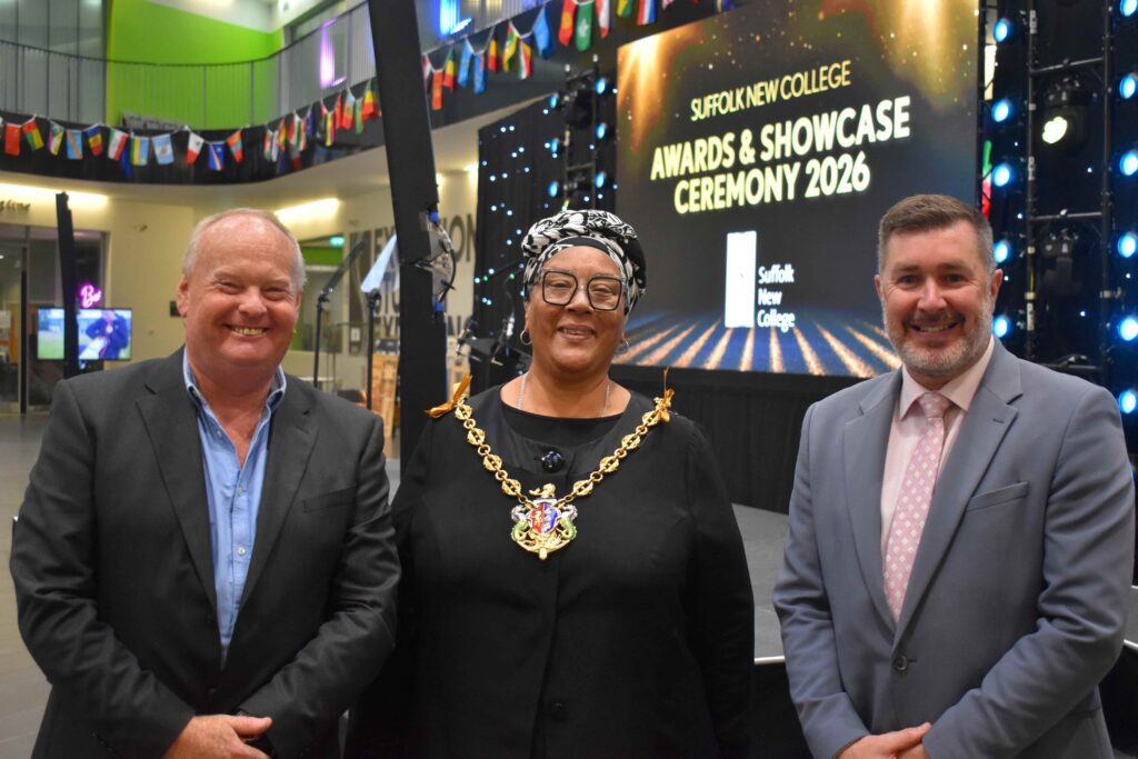 Three college staff members at Suffolk New College Awards & Showcase Ceremony 2026, smiling in front of a stage with a large screen and festive decorations.