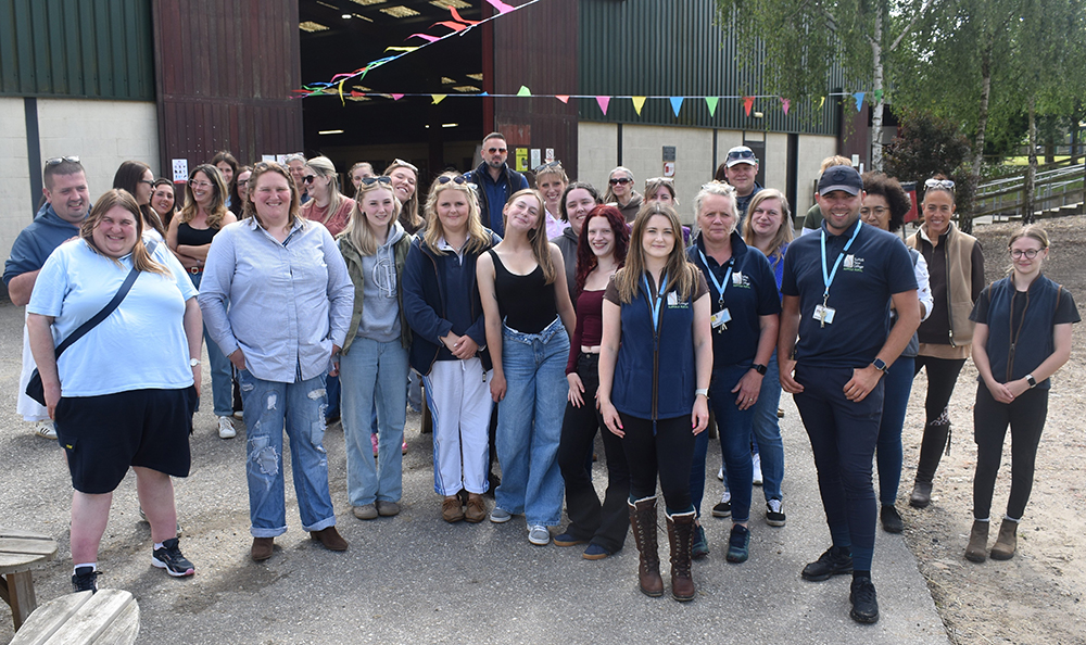 Group of students and staff celebrating at Suffolk New College's equine centre anniversary event, with festive decorations and outdoor setting.