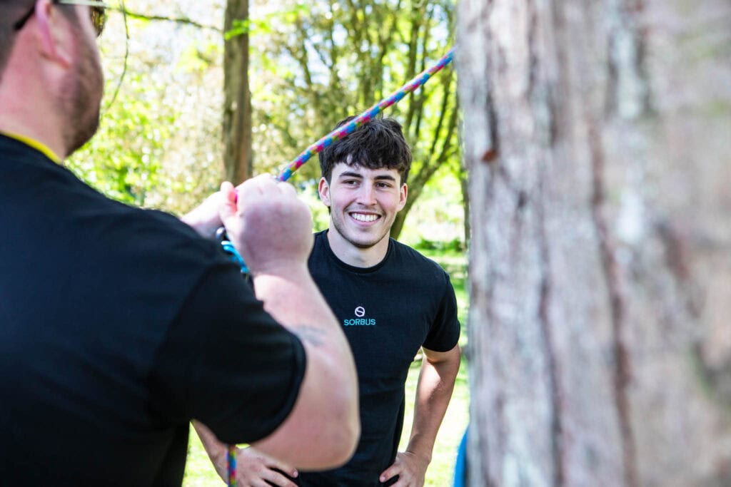 Two young men participating in outdoor team-building activities at Suffolk New College, engaging in a fun and educational experience in a lush, green forest setting.
