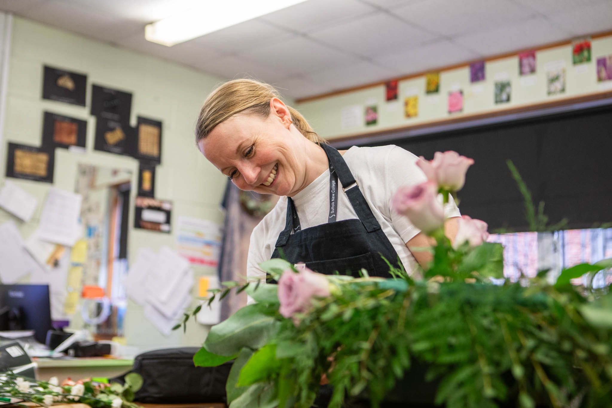 Happy female student working on floral arrangements in a classroom at Suffolk New College, focusing on floristry skills and creative design.