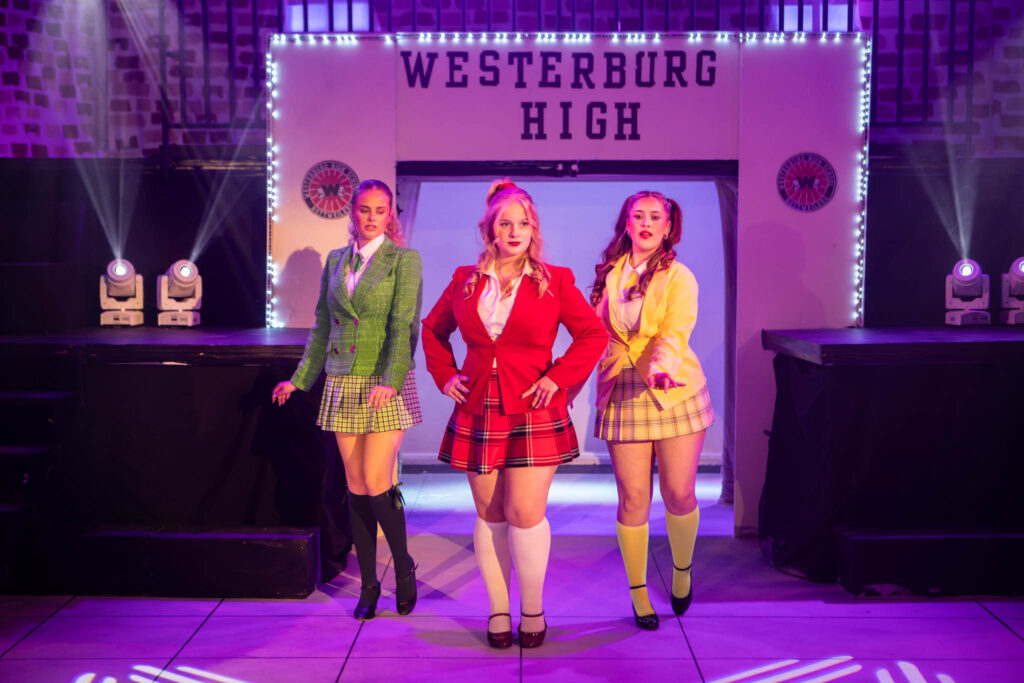 Students performing on stage at Suffolk New College, showcasing a theatrical production of Westbury High, with vibrant costumes and stage lighting.