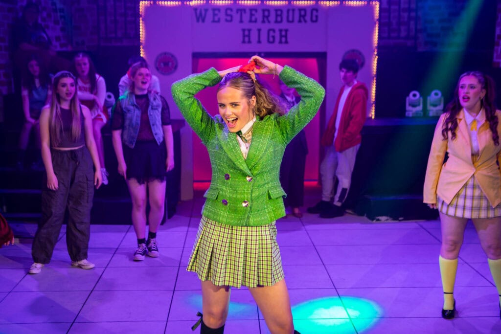 A lively scene from a college theatre production at Suffolk New College, featuring students in colourful costumes performing on stage with vibrant lighting.