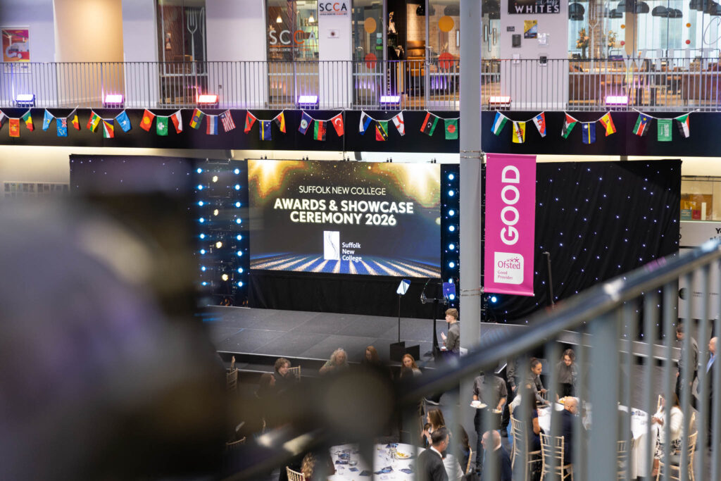 Students and staff attending the Suffolk New College awards and showcase ceremony 2026, held in a modern indoor venue with a large digital screen and colourful decorations.