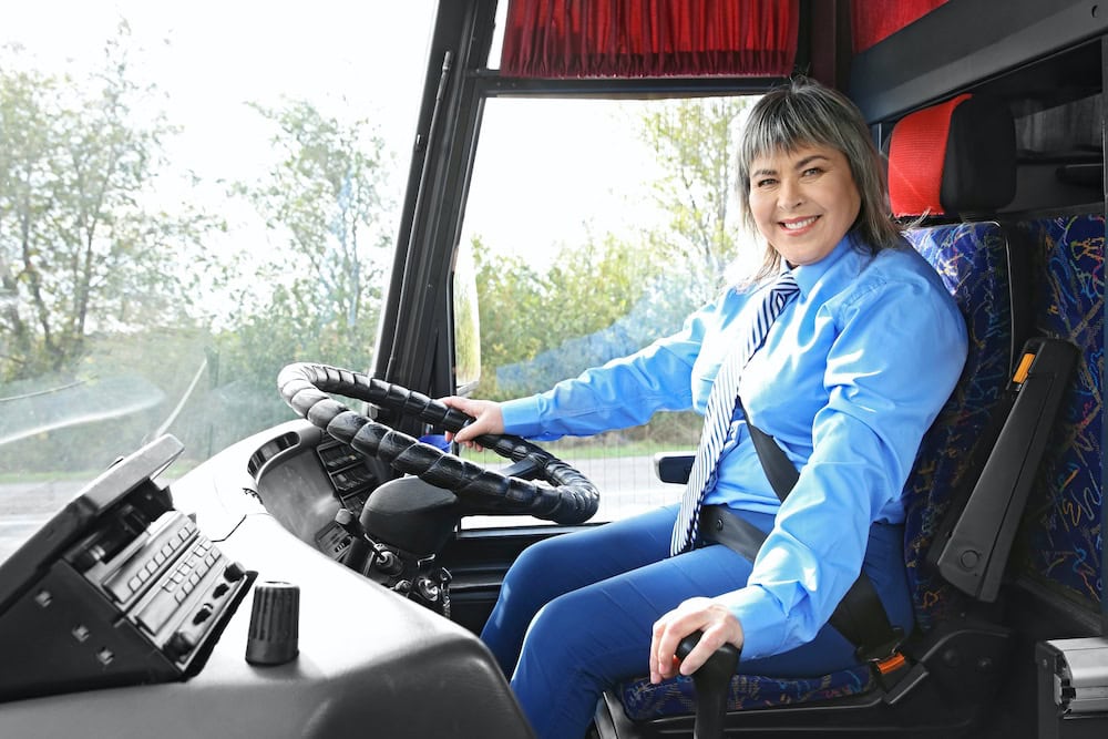 Young woman smiling in a blue uniform sitting in the driver's seat of a large vehicle, ready for driver training at Suffolk New College.