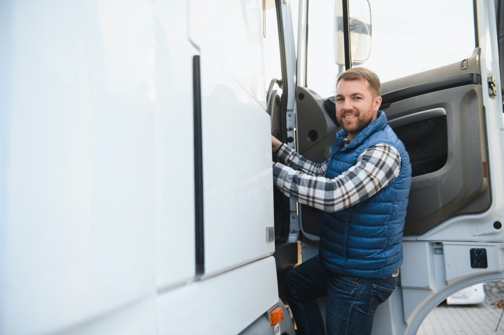 A smiling man in casual clothing and a blue vest preparing to drive a large commercial vehicle at Suffolk New College, highlighting driver training programs.