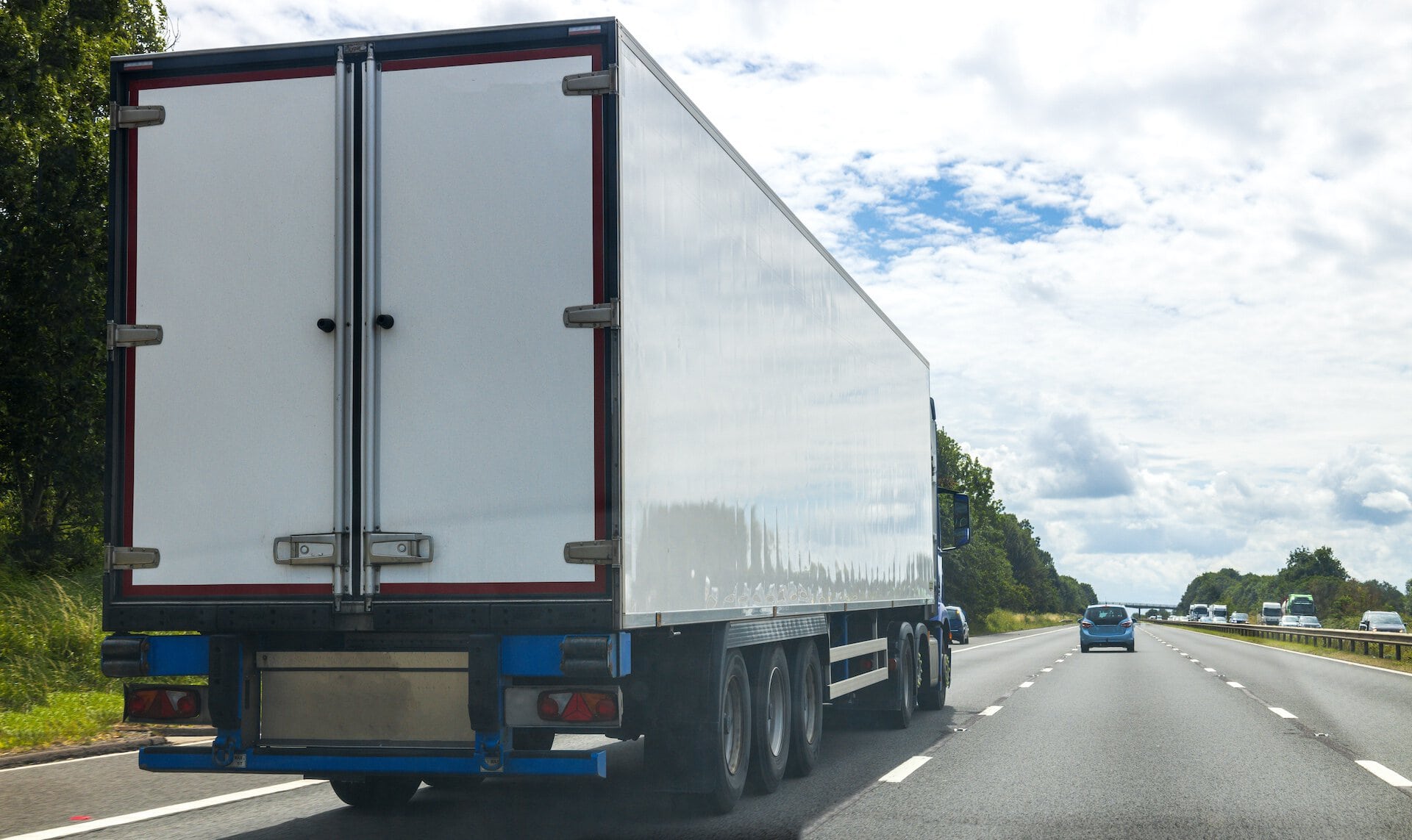 A large white delivery truck driving on a multi-lane highway with a partly cloudy sky and other vehicles in the background, representing transportation and logistics.