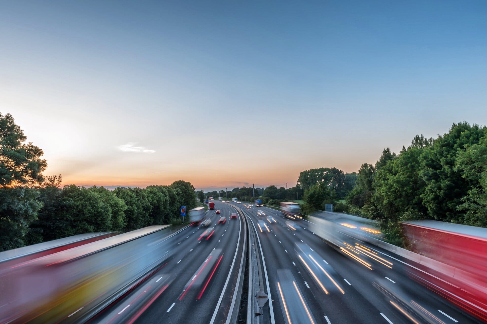 A view of a busy highway near Suffolk New College during sunset, with moving vehicles and lush green trees, highlighting education and transportation in Suffolk.