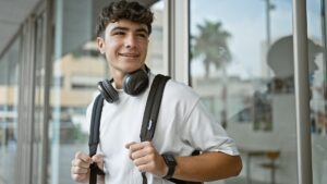 A smiling young male student with a backpack and headphones, standing outside Suffolk New College, showcasing a vibrant learning environment and student life.
