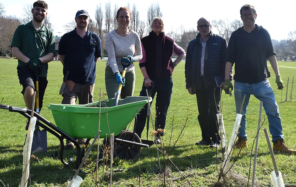 Group of Suffolk New College students and staff planting trees in a green field as part of a community project with Woodbridge Council.
