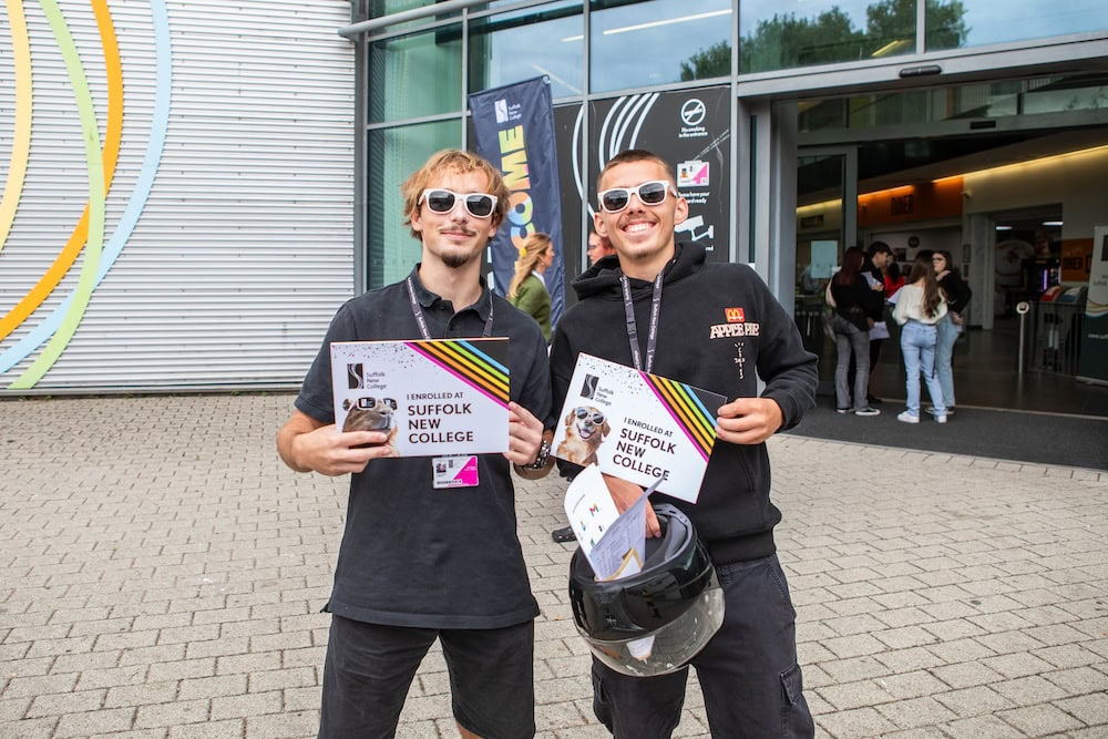 Two students smiling outside Suffolk New College holding enrolment brochures during open day event.
