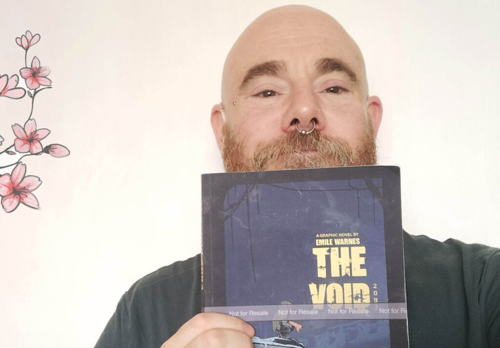 Bald male author with tattoos holding his debut book 'The Void' in front of a plain background with pink floral wall art, promoting local literary achievement.